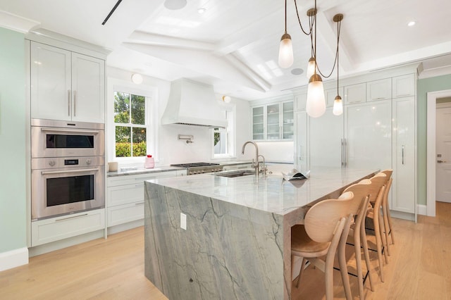 kitchen with a large island, light stone counters, sink, hanging light fixtures, and custom range hood