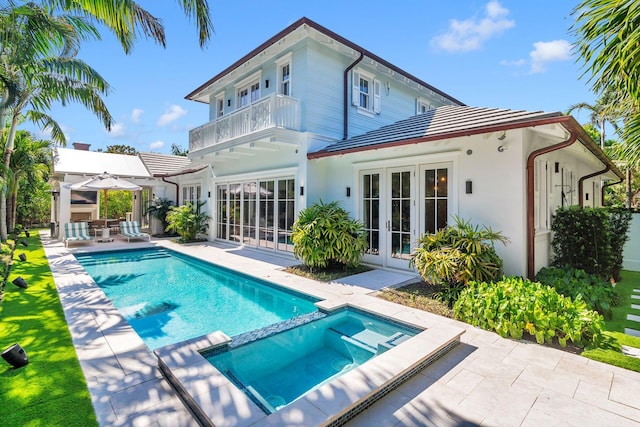 rear view of property with a balcony, a swimming pool with hot tub, french doors, and a patio area