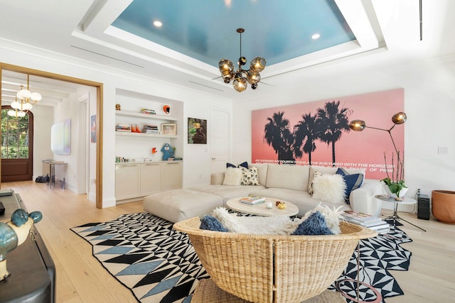 living room featuring built in shelves, an inviting chandelier, a tray ceiling, and light hardwood / wood-style flooring