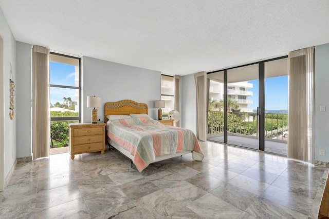 bedroom with access to outside, multiple windows, floor to ceiling windows, and a textured ceiling