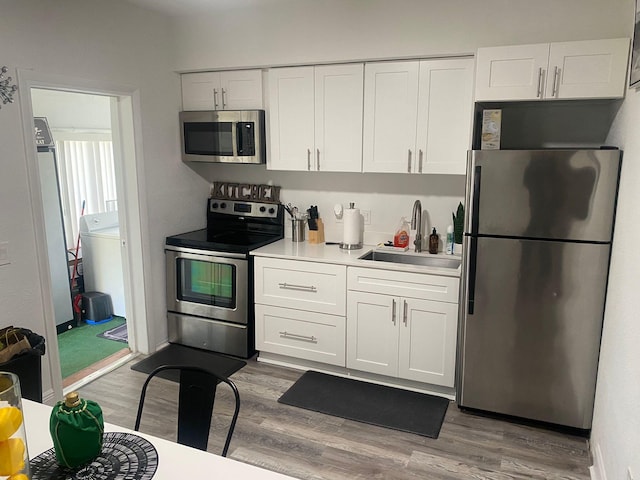 kitchen with wood finished floors, appliances with stainless steel finishes, a sink, and white cabinets