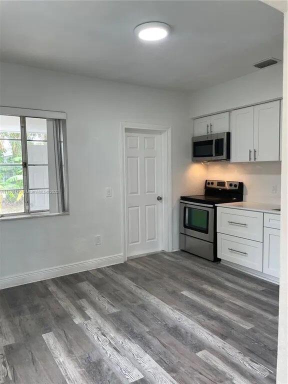 kitchen with stainless steel appliances, visible vents, dark wood-style floors, and white cabinetry