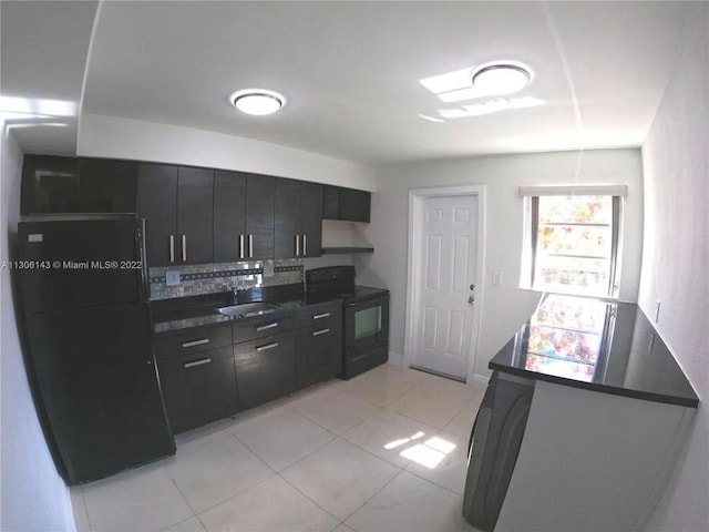 kitchen featuring dark countertops, black / electric stove, dark cabinetry, wall chimney range hood, and a sink