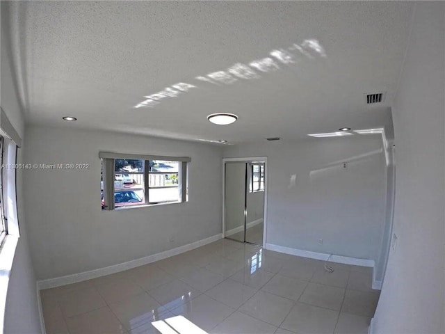 empty room featuring visible vents, a textured ceiling, baseboards, and tile patterned floors