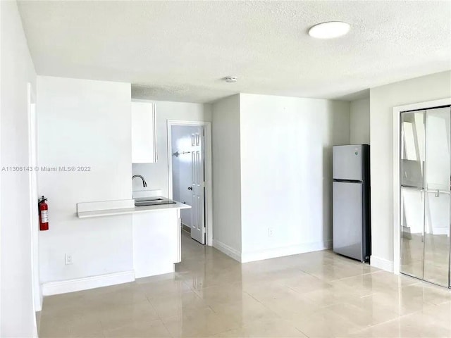 kitchen featuring freestanding refrigerator, a sink, a textured ceiling, and baseboards