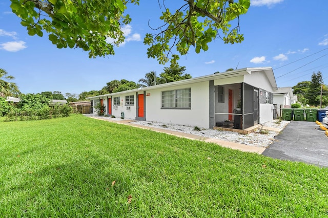 ranch-style home with a front yard, a sunroom, fence, and stucco siding