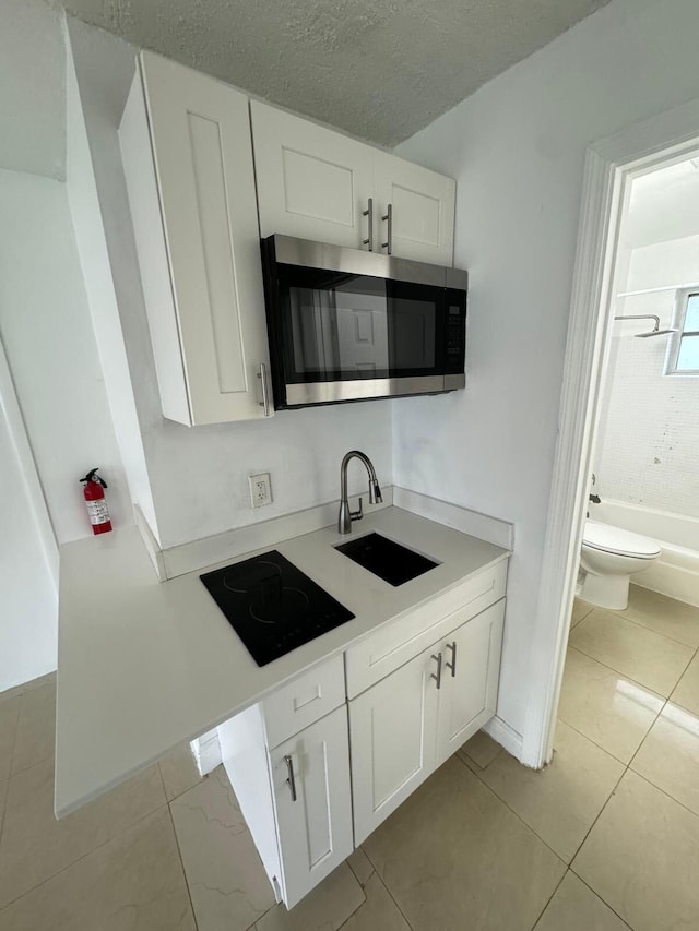 kitchen featuring white cabinets, stainless steel microwave, black electric cooktop, light countertops, and a sink