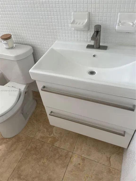 bathroom featuring tile patterned flooring, backsplash, vanity, and toilet