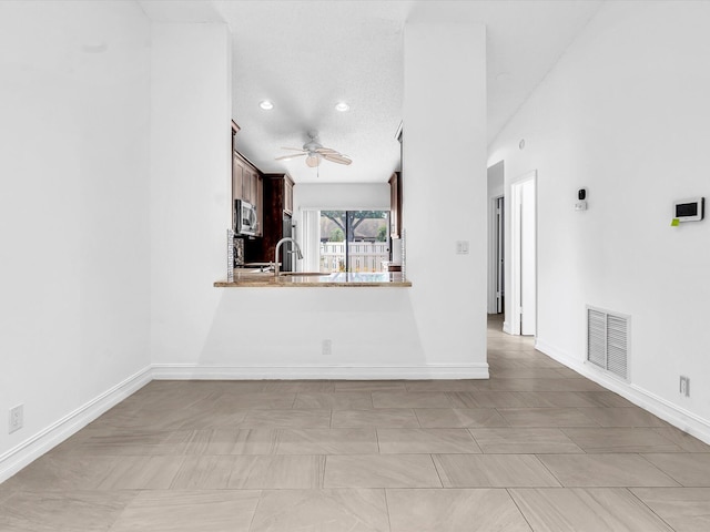 unfurnished living room with ceiling fan, light tile patterned floors, a textured ceiling, and sink