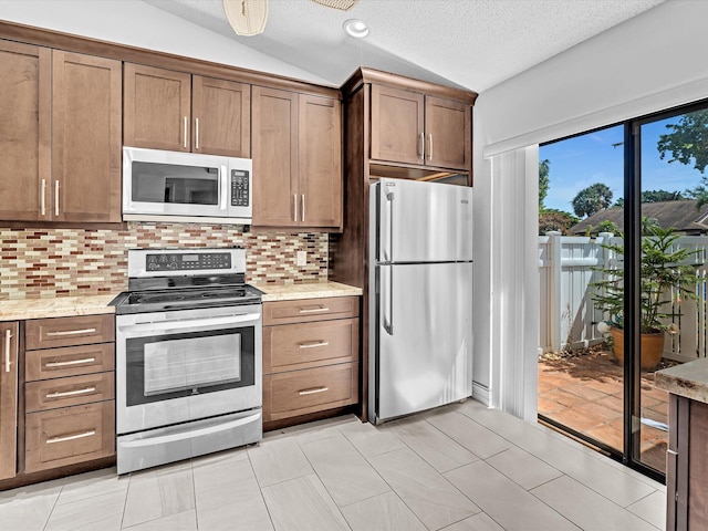 kitchen with a textured ceiling, lofted ceiling, stainless steel appliances, backsplash, and light stone countertops