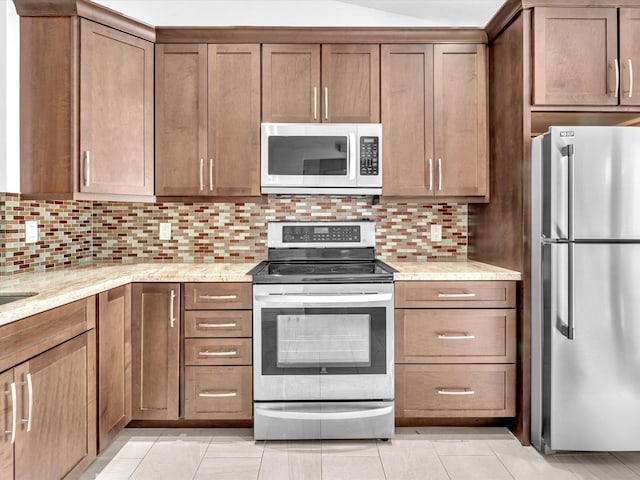 kitchen featuring light stone countertops, light tile patterned flooring, appliances with stainless steel finishes, and decorative backsplash