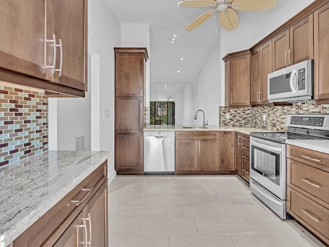 kitchen featuring ceiling fan, light stone counters, sink, stainless steel appliances, and decorative backsplash