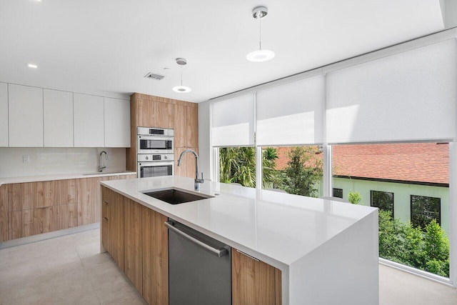 kitchen with pendant lighting, appliances with stainless steel finishes, a kitchen island with sink, sink, and white cabinets