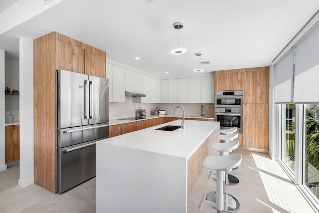 kitchen featuring an island with sink, a kitchen bar, stainless steel appliances, sink, and white cabinetry