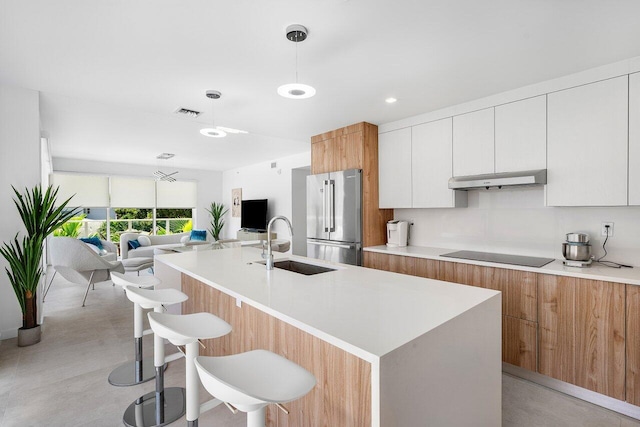 kitchen featuring high end fridge, decorative light fixtures, sink, black electric cooktop, and white cabinets