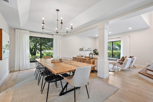 dining area featuring ornate columns, light hardwood / wood-style floors, a raised ceiling, and a chandelier