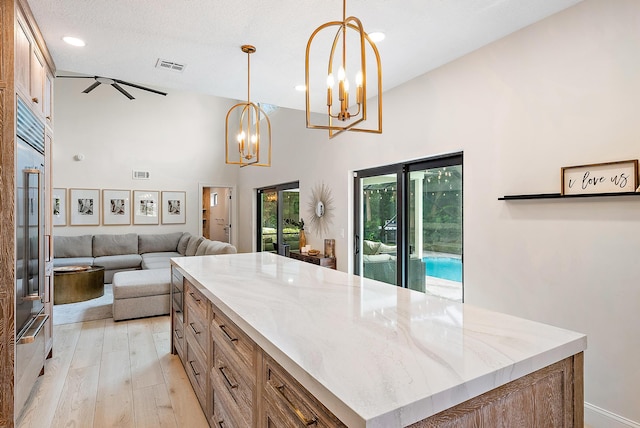 kitchen featuring a kitchen island, light hardwood / wood-style floors, hanging light fixtures, a textured ceiling, and high vaulted ceiling