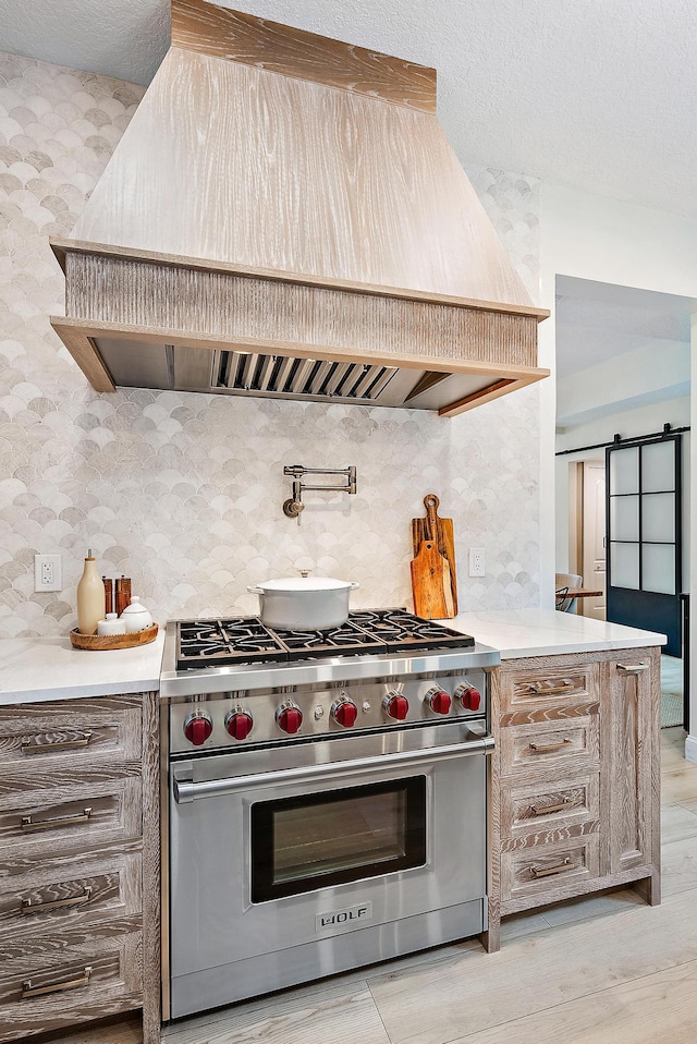 kitchen featuring premium range hood, a textured ceiling, a barn door, light hardwood / wood-style flooring, and premium range