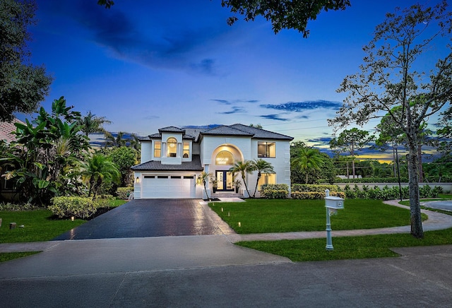 view of front facade featuring driveway, an attached garage, a lawn, and stucco siding