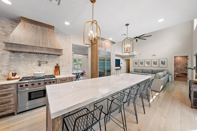 kitchen featuring premium appliances, a kitchen bar, custom range hood, light stone counters, and light hardwood / wood-style flooring