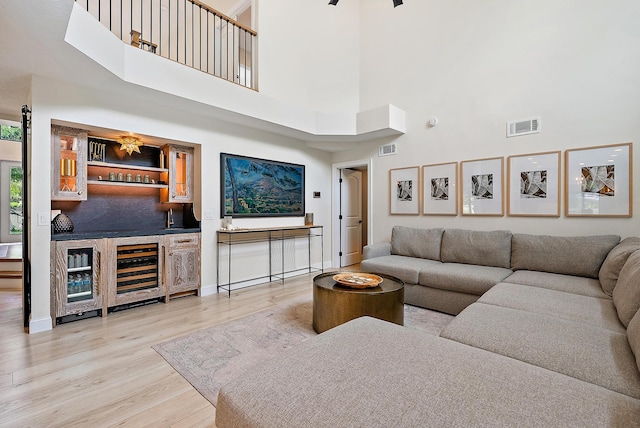 living room featuring wine cooler, bar, a towering ceiling, and light hardwood / wood-style flooring