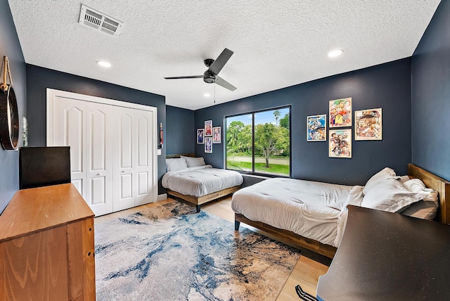 bedroom with a closet, a textured ceiling, light wood-type flooring, and ceiling fan