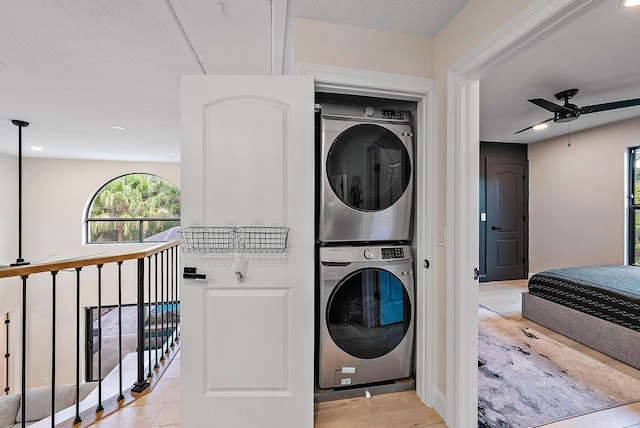 washroom with stacked washer and clothes dryer, a textured ceiling, light hardwood / wood-style floors, and ceiling fan