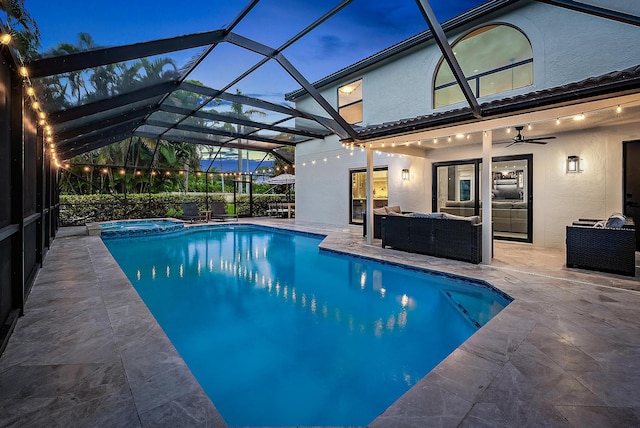 pool at dusk with an outdoor hangout area, a patio area, glass enclosure, and ceiling fan