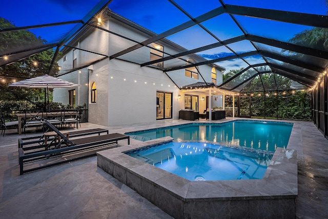 pool at dusk featuring a patio area, a lanai, and an in ground hot tub