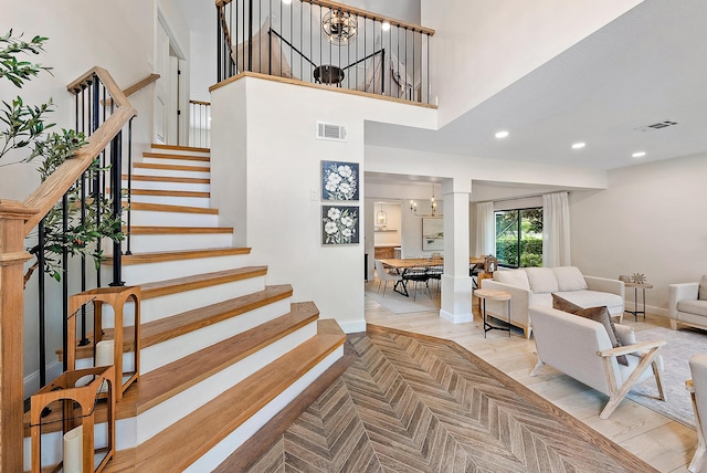 stairs with a chandelier, wood-type flooring, and a high ceiling