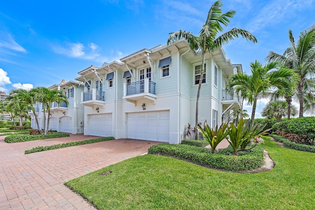 view of front facade featuring driveway, a garage, a balcony, a front yard, and stucco siding