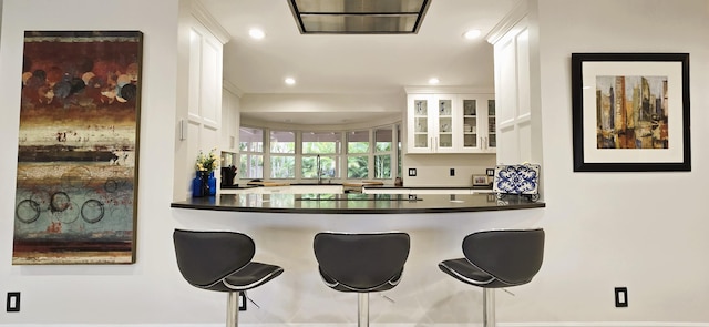 kitchen with white cabinets, a breakfast bar area, stovetop, and kitchen peninsula