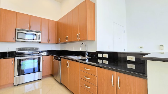 kitchen featuring dark stone counters, stainless steel appliances, light tile patterned floors, and sink