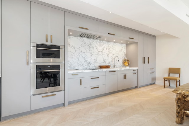 kitchen with stainless steel double oven, light stone counters, sink, black electric cooktop, and tasteful backsplash