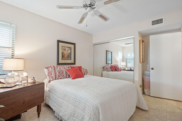 bedroom with a closet, ceiling fan, light tile patterned floors, and a textured ceiling