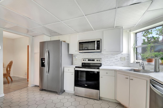 kitchen with appliances with stainless steel finishes, white cabinetry, sink, a drop ceiling, and decorative backsplash