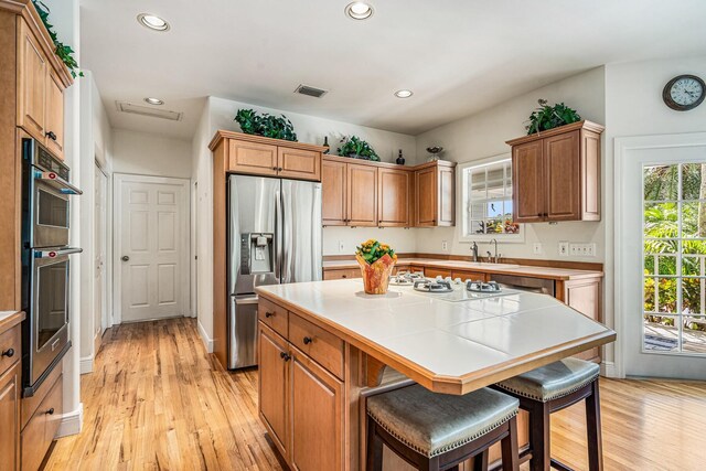 kitchen with appliances with stainless steel finishes, a kitchen breakfast bar, a center island, light hardwood / wood-style flooring, and tile counters