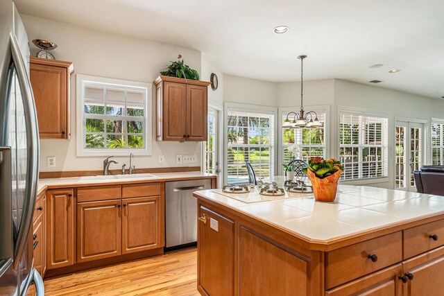 kitchen featuring appliances with stainless steel finishes, tile countertops, light wood-type flooring, an inviting chandelier, and sink