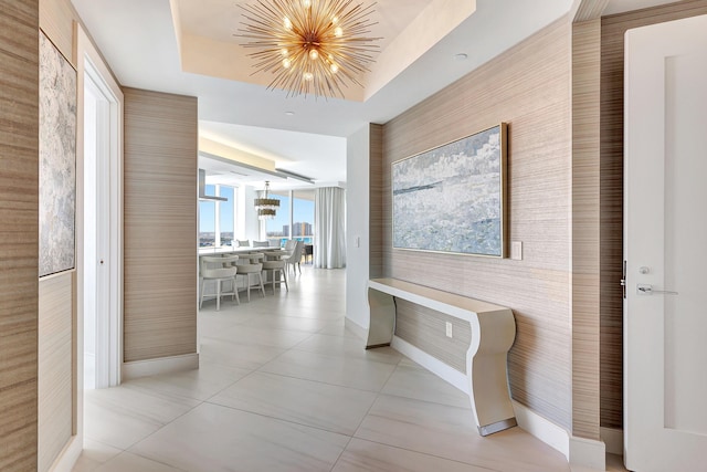 hall with light tile patterned floors, a tray ceiling, baseboards, and an inviting chandelier