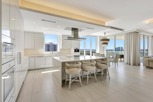 kitchen featuring decorative light fixtures, white cabinetry, island range hood, and a center island