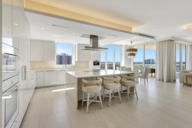 kitchen with visible vents, a view of city, modern cabinets, tasteful backsplash, and island range hood