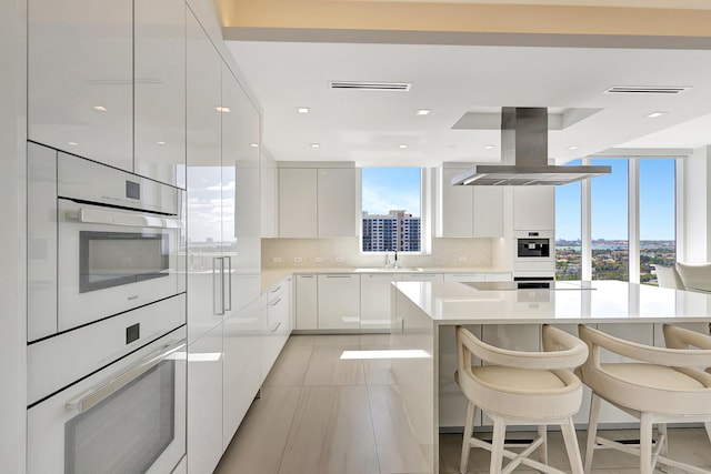 kitchen with a sink, backsplash, island exhaust hood, white cabinetry, and modern cabinets