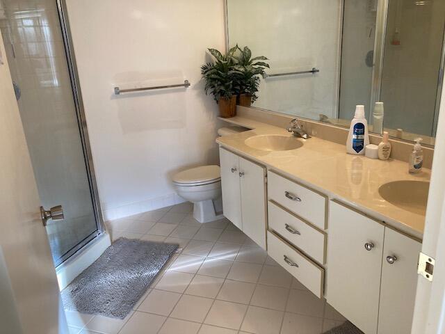 bathroom featuring a stall shower, toilet, a sink, tile patterned flooring, and double vanity