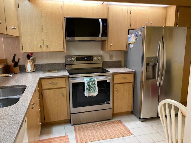 kitchen featuring a sink, backsplash, appliances with stainless steel finishes, and light tile patterned floors