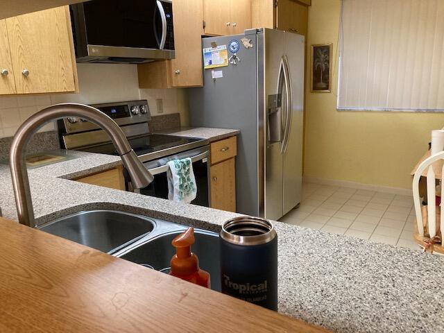 kitchen featuring light countertops, light tile patterned floors, baseboards, backsplash, and appliances with stainless steel finishes