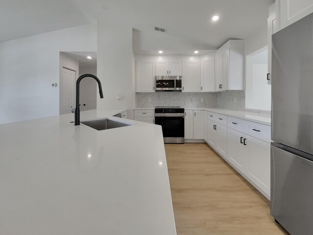 kitchen featuring light wood-type flooring, white cabinetry, stainless steel appliances, sink, and vaulted ceiling