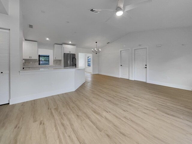 unfurnished living room with vaulted ceiling, ceiling fan with notable chandelier, and light hardwood / wood-style floors