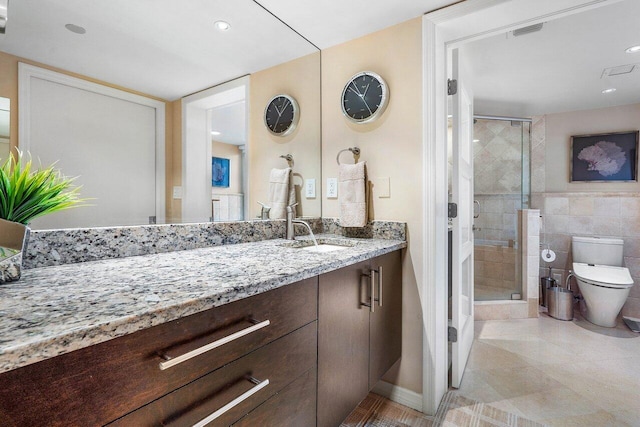 bathroom with toilet, tile patterned flooring, a shower with door, vanity, and tile walls