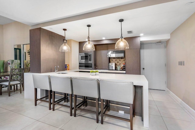 kitchen featuring pendant lighting, stainless steel appliances, a kitchen breakfast bar, kitchen peninsula, and sink