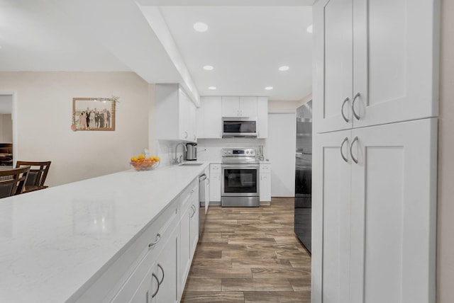 kitchen with white cabinetry, sink, light stone countertops, appliances with stainless steel finishes, and hardwood / wood-style flooring